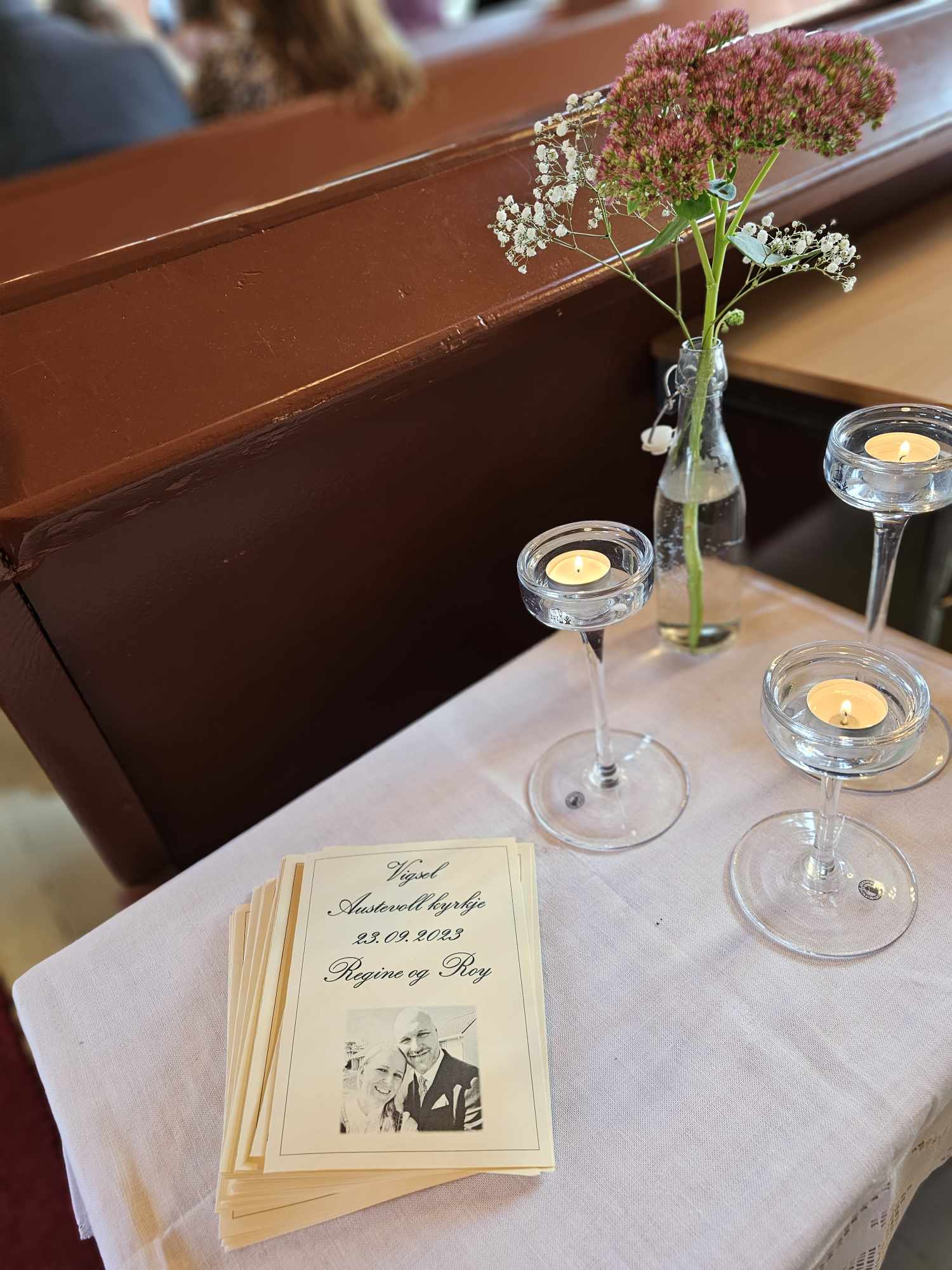 Program til vigsel som ligg på eit bord med lys og blomar på.