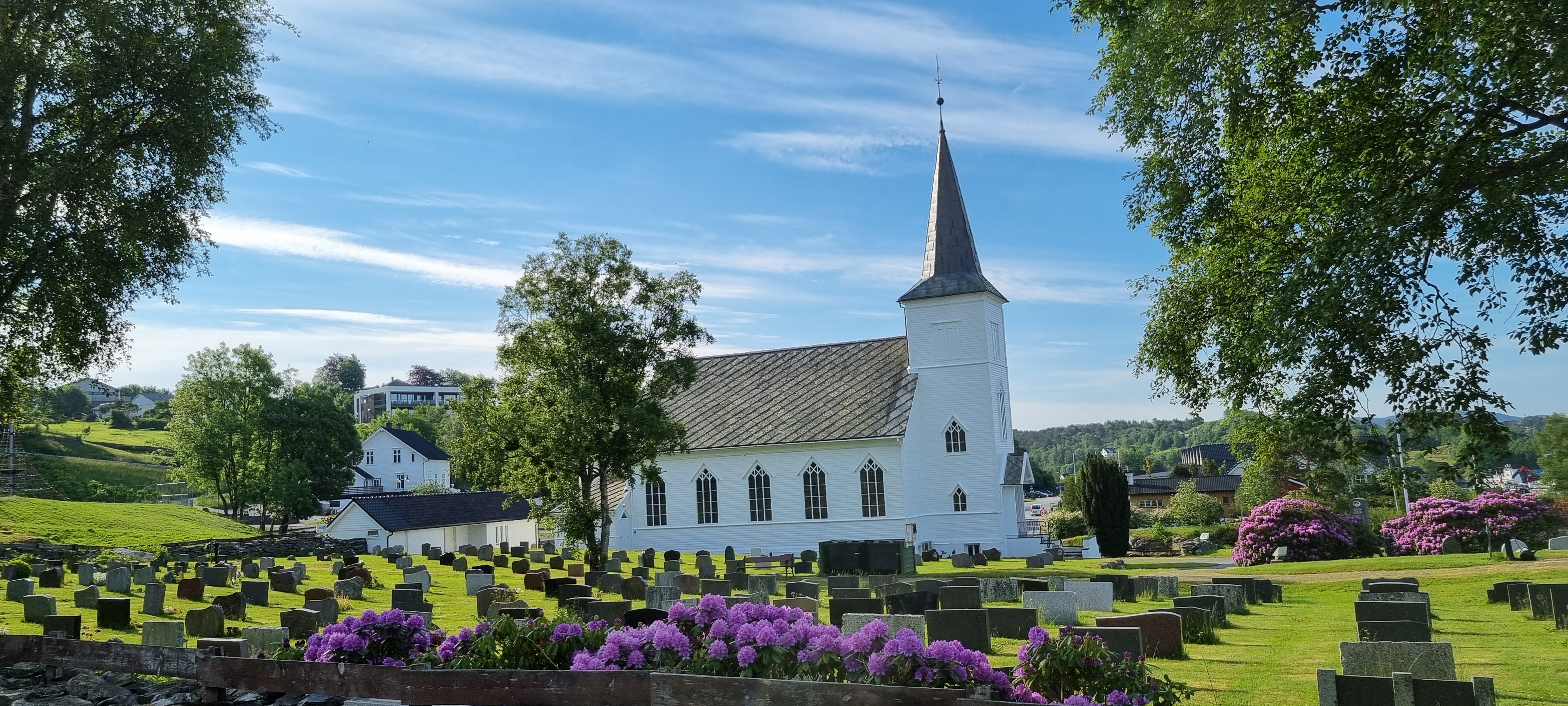 Austevoll kyrkjegard med kyrkja i bakgrunnen på ein fin vårdag